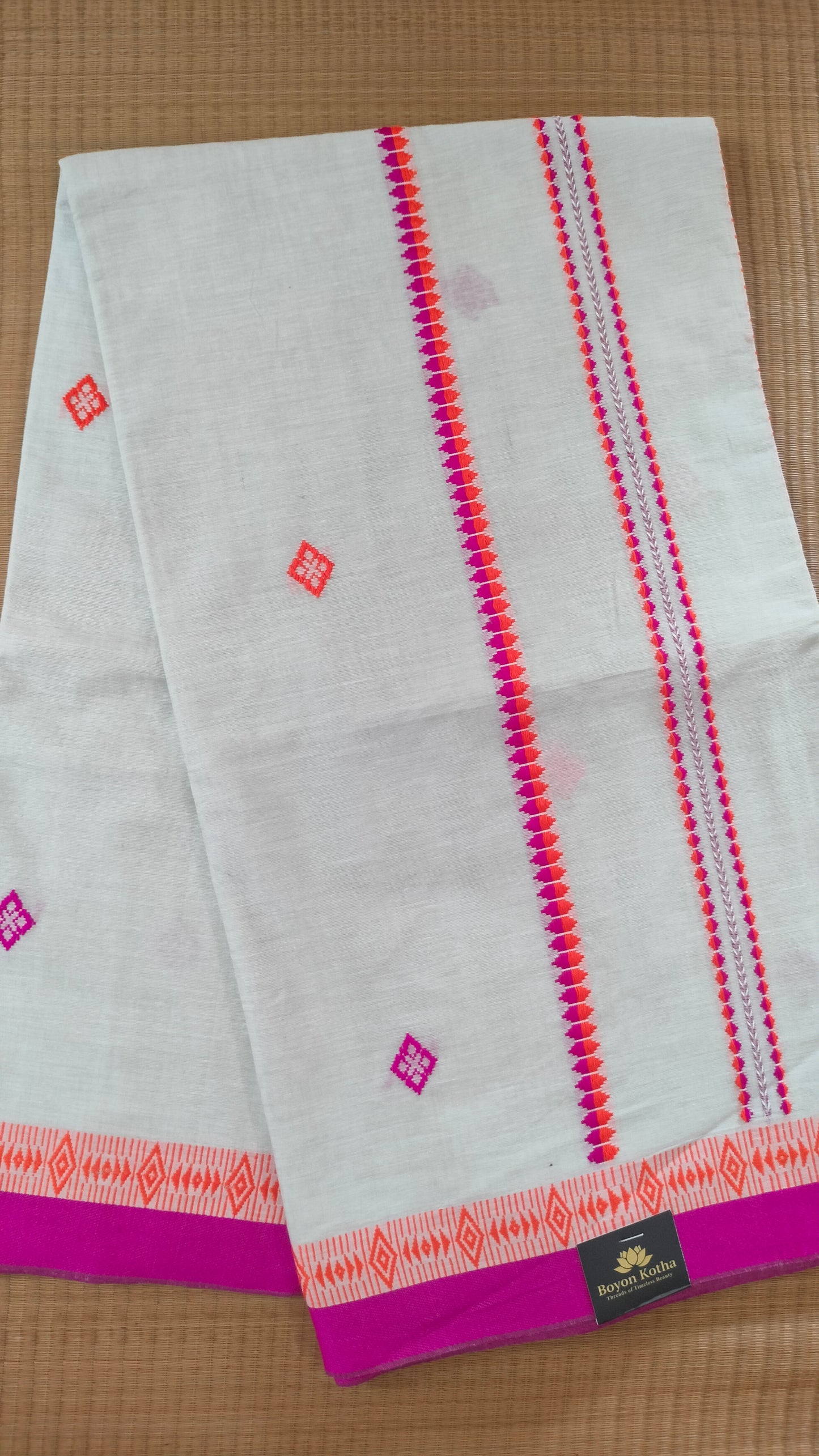 A white Dhonekhali handloom cotton saree with orange and pink woven motifs and bands on the saree. The border of the saree is pink with the inner edge having orange motifs.