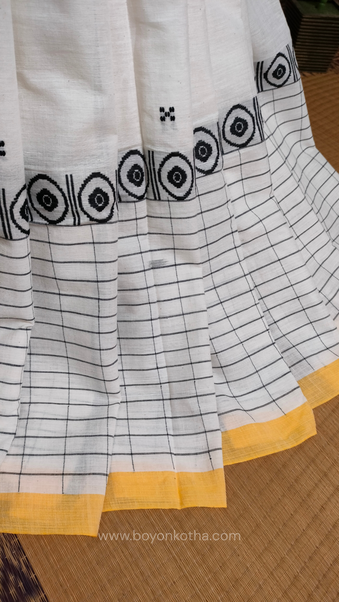 White Dhonekhali handloom cotton saree featuring a delicate yellow border and intricate woven black and yellow motifs. 