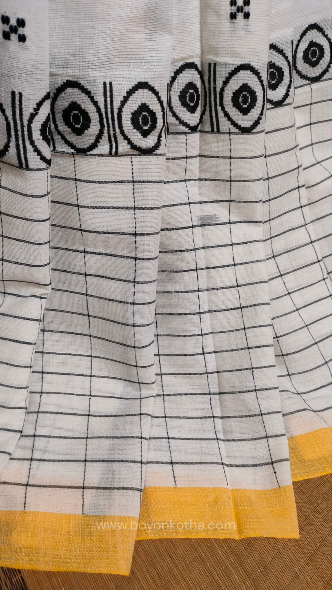 White Dhonekhali handloom cotton saree featuring a delicate yellow border and intricate woven black and yellow motifs. 