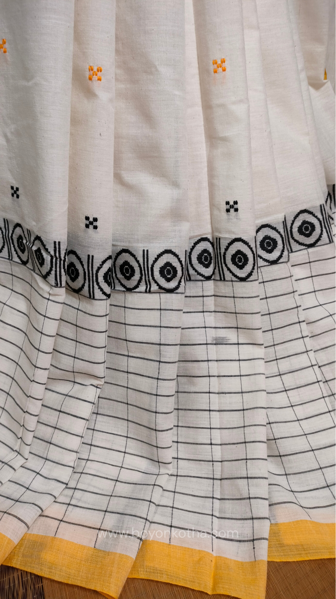 White Dhonekhali handloom cotton saree featuring a delicate yellow border and intricate woven black and yellow motifs. 