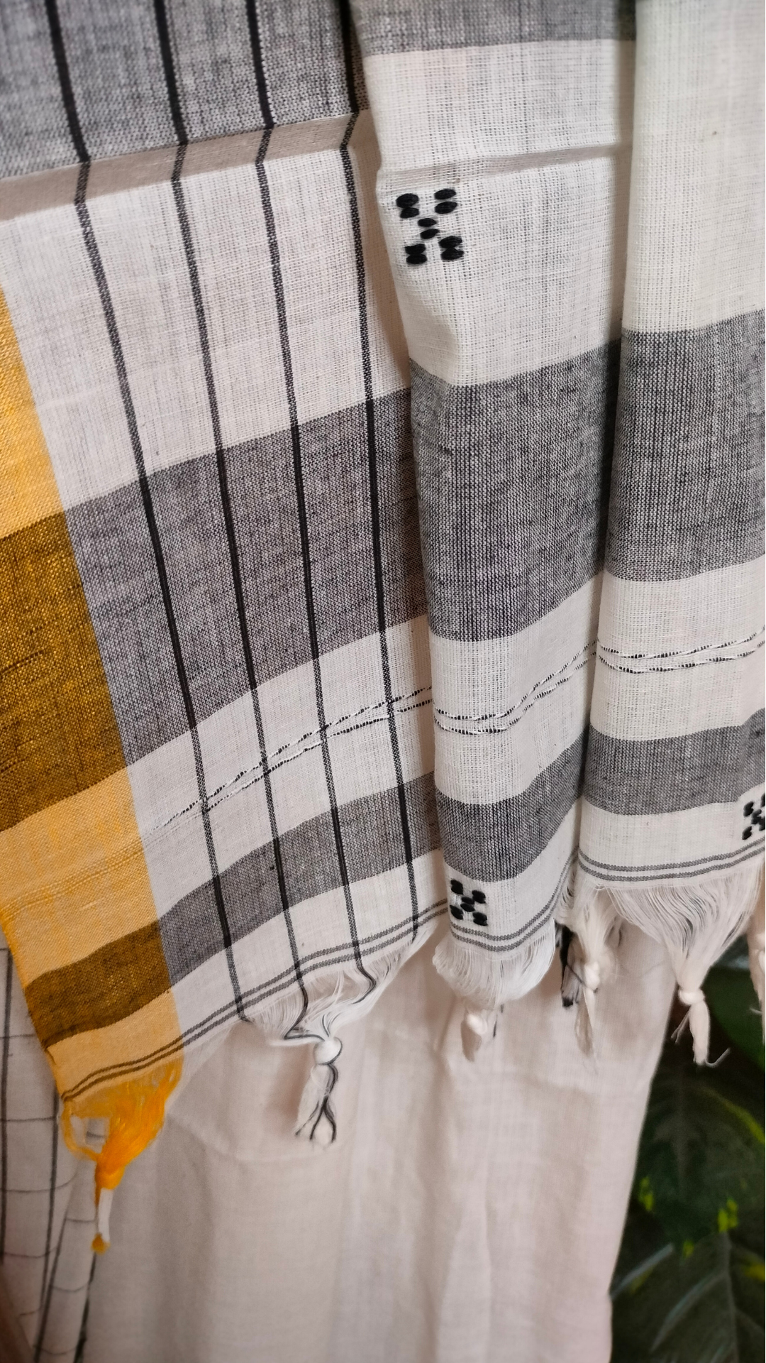 White Dhonekhali handloom cotton saree featuring a delicate yellow border and intricate woven black and yellow motifs. 