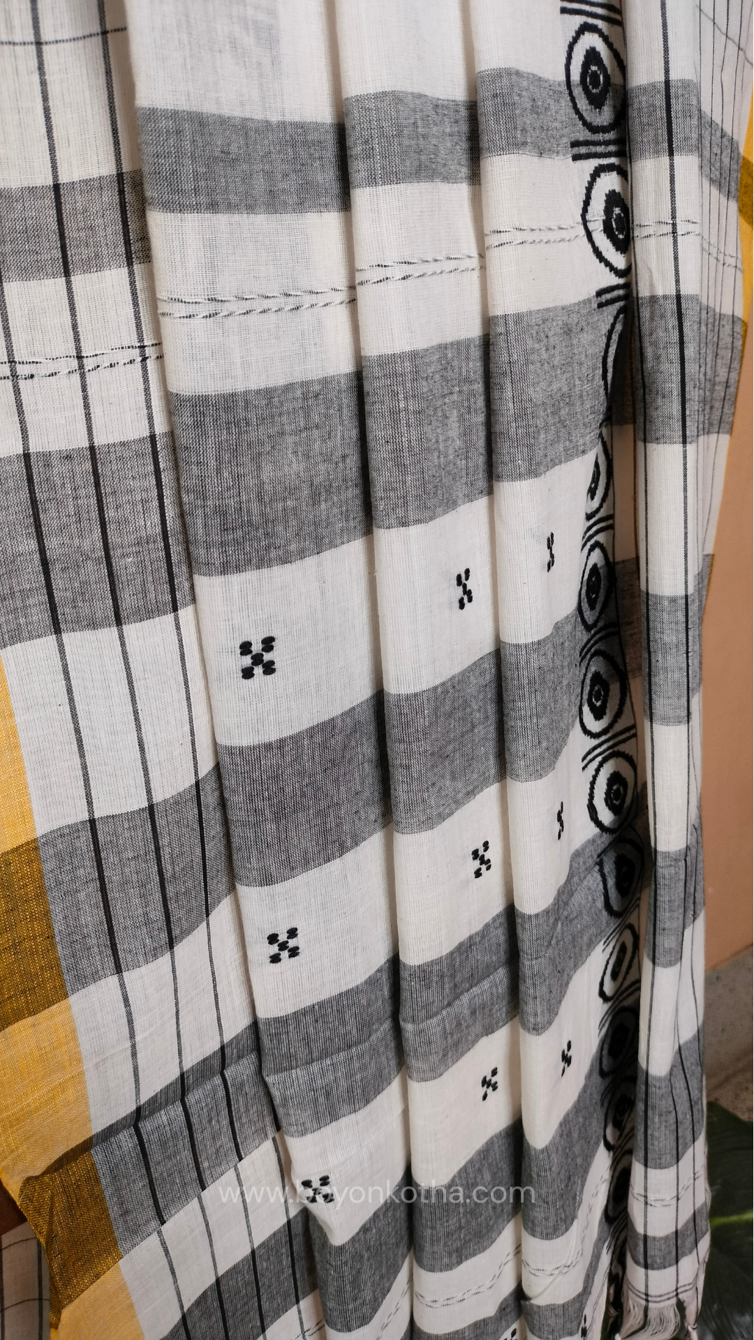 White Dhonekhali handloom cotton saree featuring a delicate yellow border and intricate woven black and yellow motifs. 