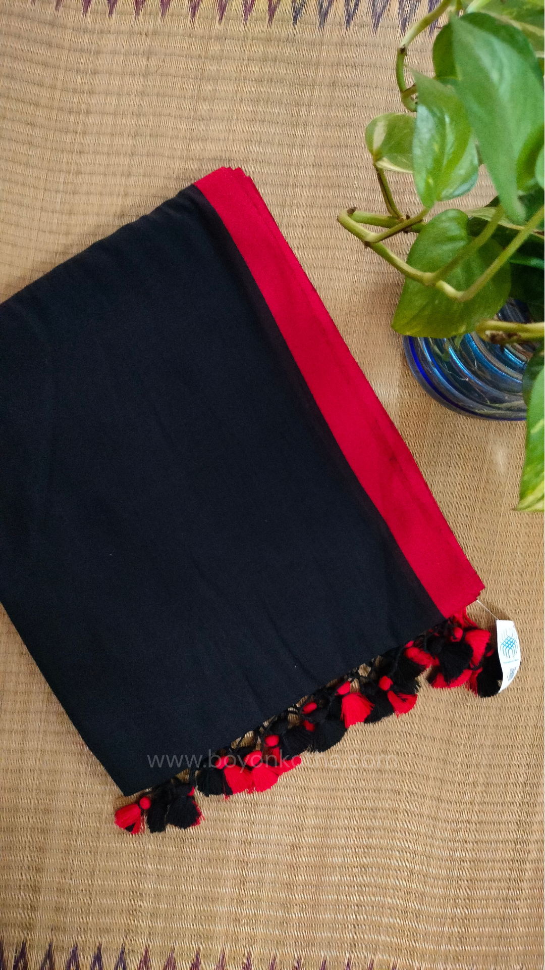 Black handwoven mul cotton saree with red border, pallu ending in tassels. Plain handloom black saree from Bengal.