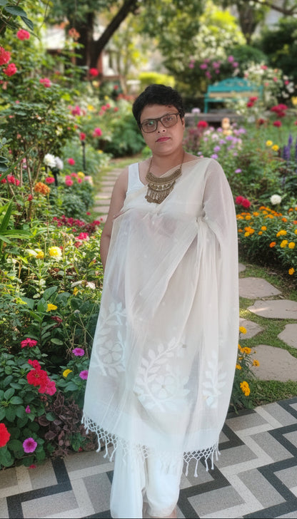 Model wearing a white mul cotton saree with jamdani motifs standing in a garden