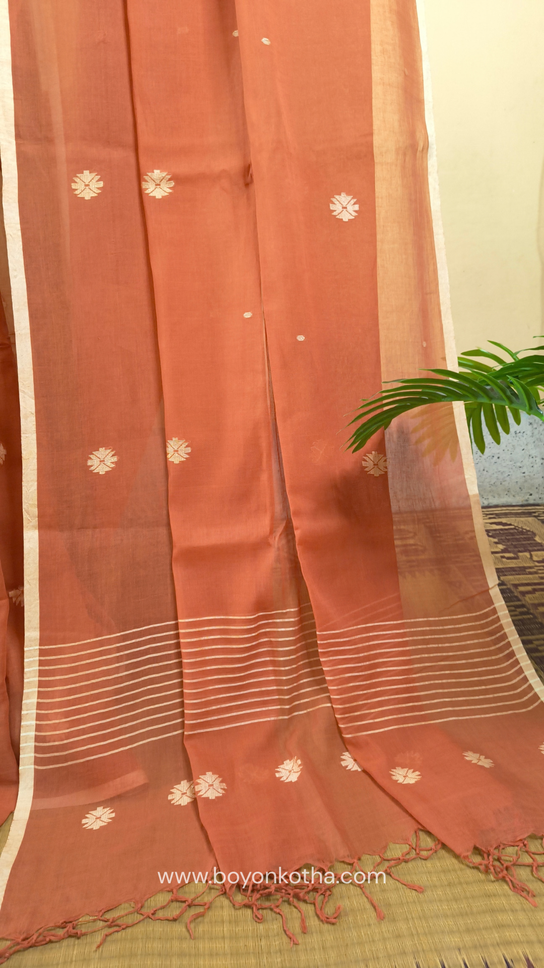 Orangish peach buttery soft handloom cotton saree, with jamdani inspired handloom jacquard woven butas all over and braided tassels. Ideal for festive mornings 