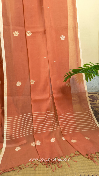 Orangish peach buttery soft handloom cotton saree, with jamdani inspired handloom jacquard woven butas all over and braided tassels. Ideal for festive mornings 
