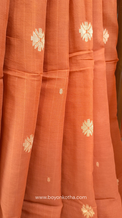 Orangish peach buttery soft handloom cotton saree, with jamdani inspired handloom jacquard woven butas all over and braided tassels. Ideal for festive mornings 
