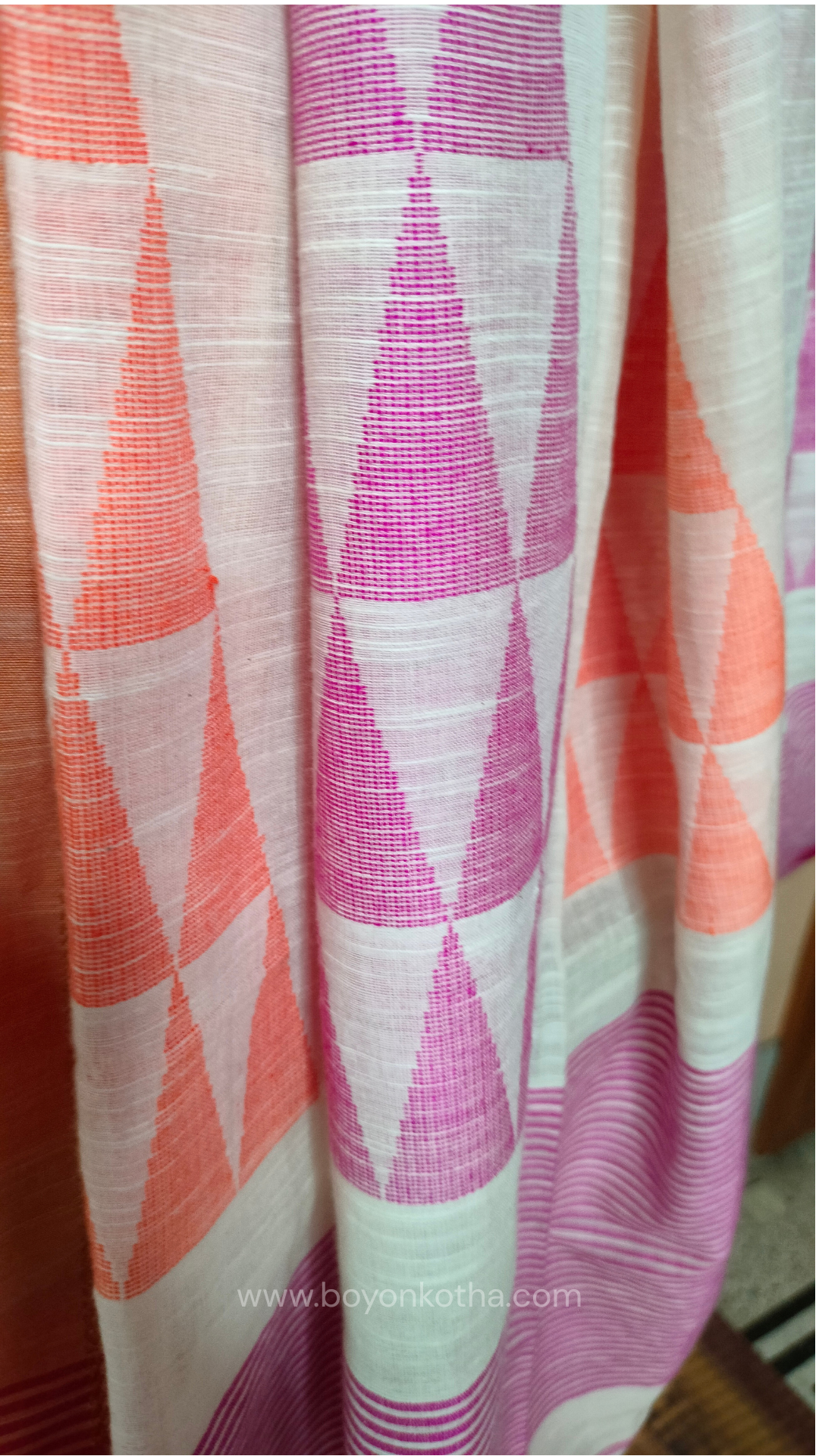 Off-white Bengal handloom cotton saree with ganga-jamuna border in orange and pink. Geometric woven motifs adorn the body, while the pallu features triangular patterns and tasseled ends. 