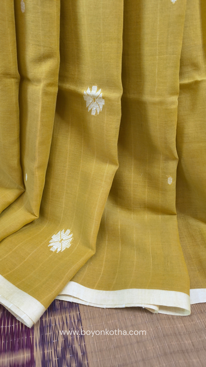 Greenish yellow buttery soft handloom cotton saree, with jamdani inspired handloom jacquard woven butas all over and braided tassels. Ideal for festive mornings 