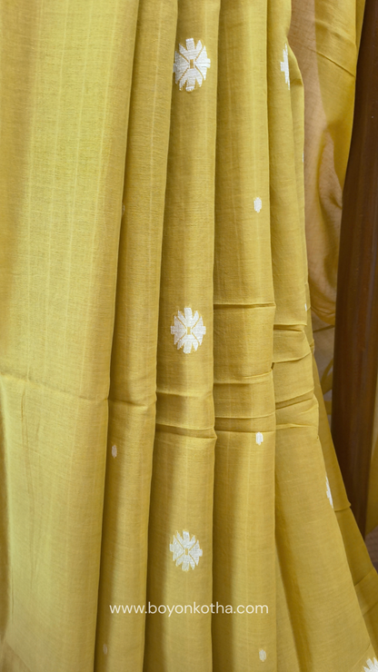 Greenish yellow buttery soft handloom cotton saree, with jamdani inspired handloom jacquard woven butas all over and braided tassels. Ideal for festive mornings 