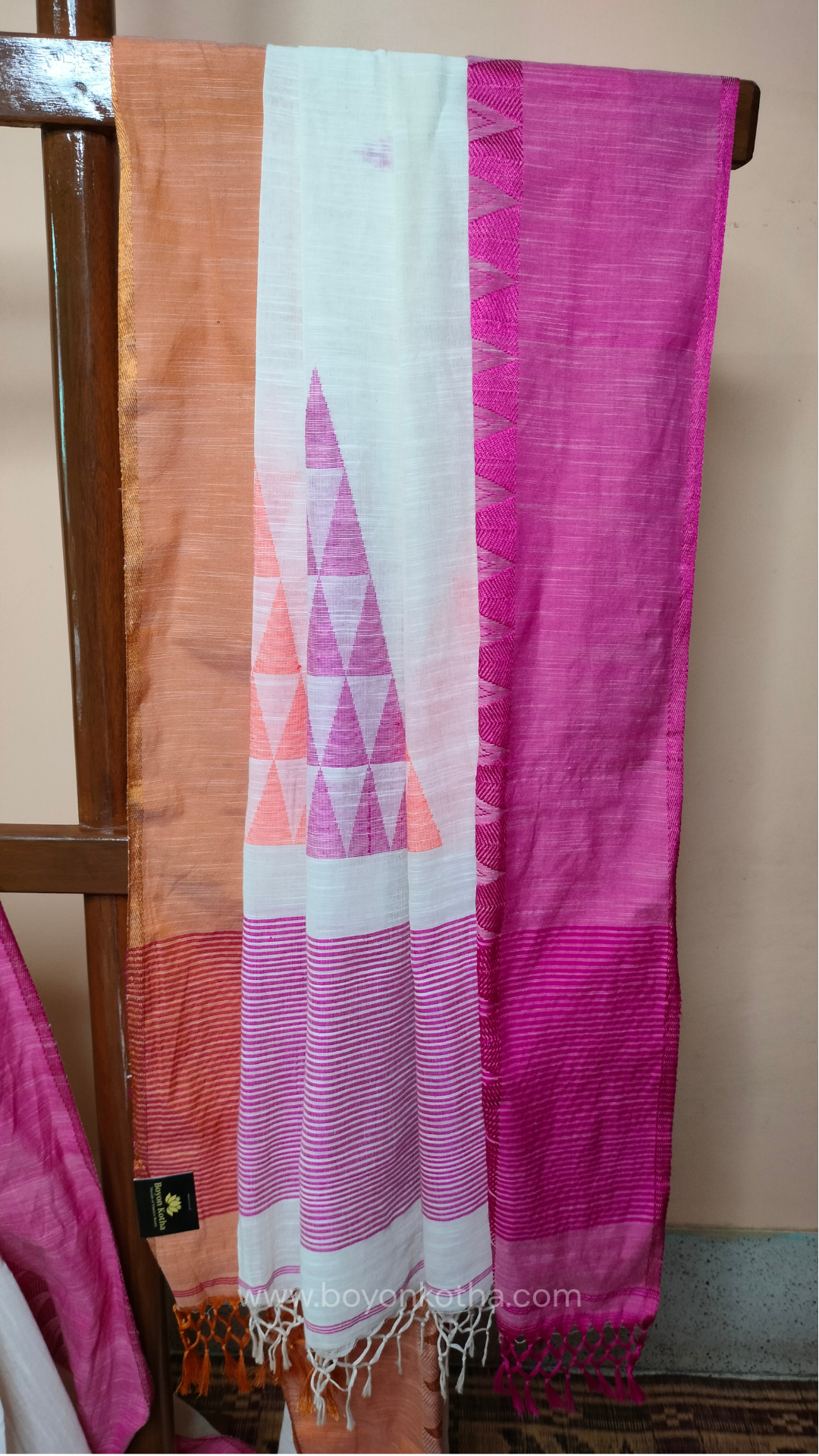 Off-white Bengal handloom cotton saree with ganga-jamuna border in orange and pink. Geometric woven motifs adorn the body, while the pallu features triangular patterns and tasseled ends. 
