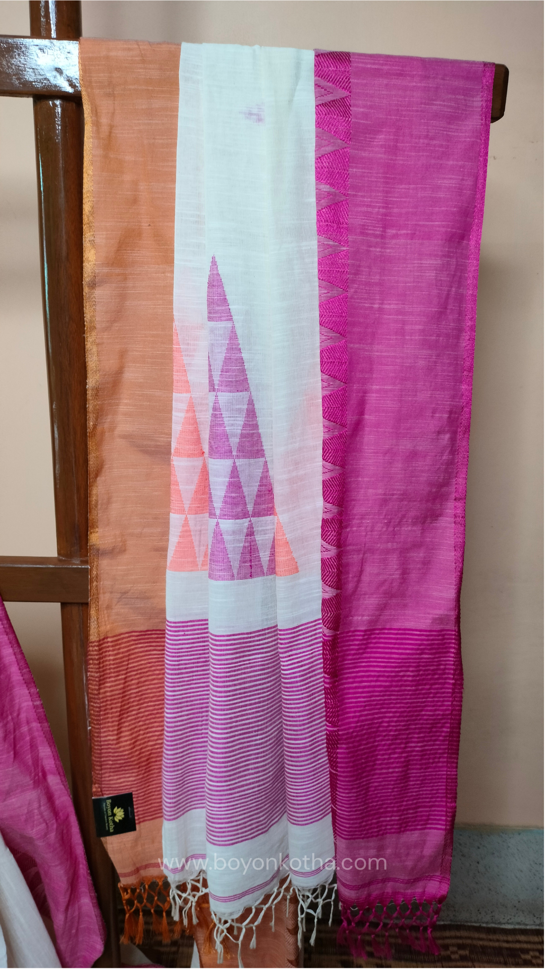 Off-white Bengal handloom cotton saree with ganga-jamuna border in orange and pink. Geometric woven motifs adorn the body, while the pallu features triangular patterns and tasseled ends. 
