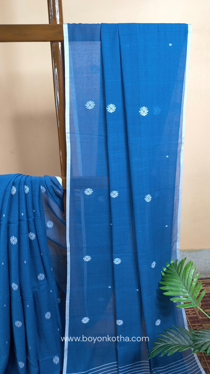Blue buttery soft handloom cotton saree, with jamdani inspired handloom jacquard woven butas all over and braided tassels. Ideal for festive mornings 