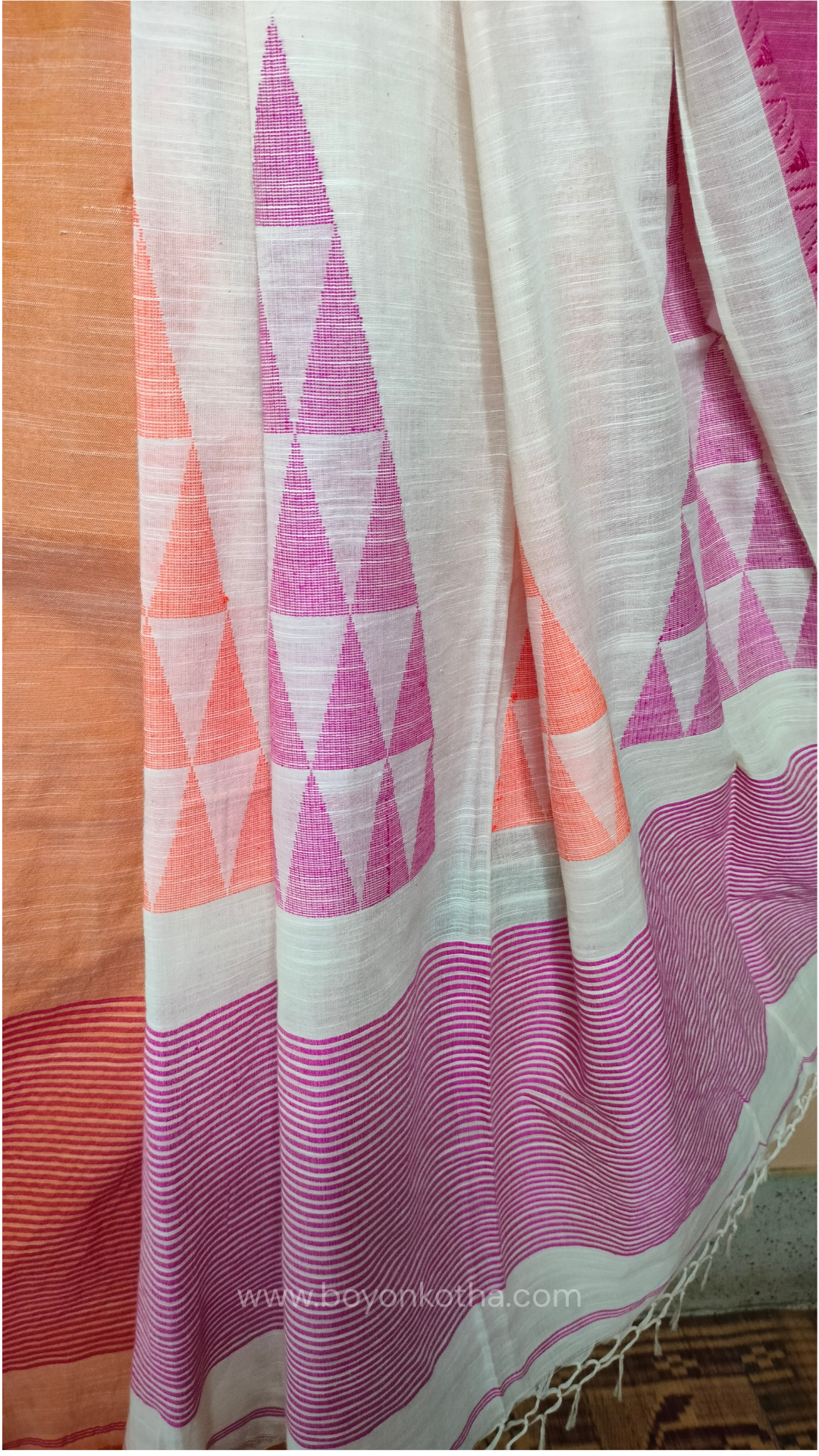 Off-white Bengal handloom cotton saree with ganga-jamuna border in orange and pink. Geometric woven motifs adorn the body, while the pallu features triangular patterns and tasseled ends. 