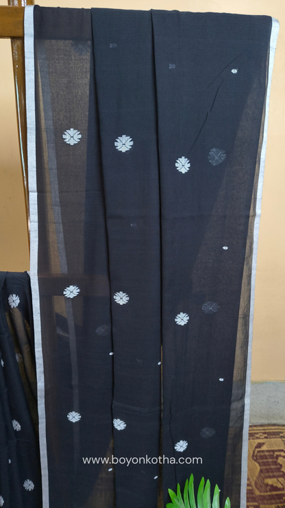 Black buttery soft handloom cotton saree, with jamdani inspired handloom jacquard woven butas all over and braided tassels. Ideal for festive mornings 