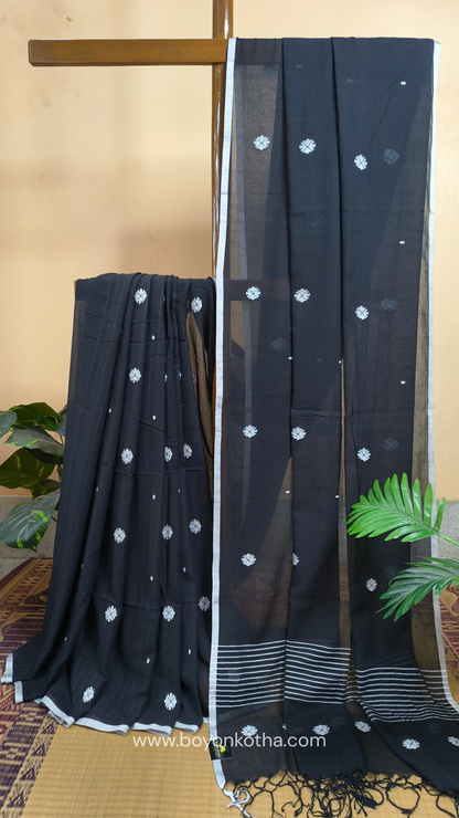 Black buttery soft handloom cotton saree, with jamdani inspired handloom jacquard woven butas all over and braided tassels. Ideal for festive mornings 