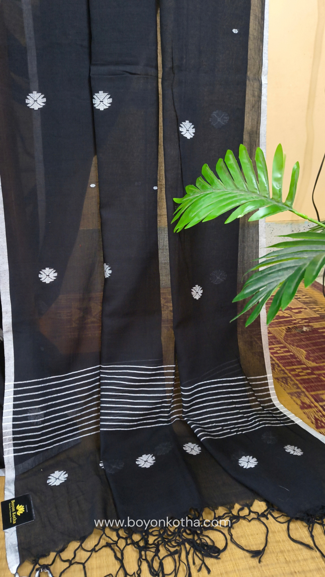 Black buttery soft handloom cotton saree, with jamdani inspired handloom jacquard woven butas all over and braided tassels. Ideal for festive mornings 