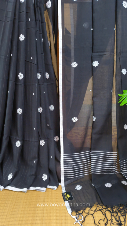 Black buttery soft handloom cotton saree, with jamdani inspired handloom jacquard woven butas all over and braided tassels. Ideal for festive mornings 