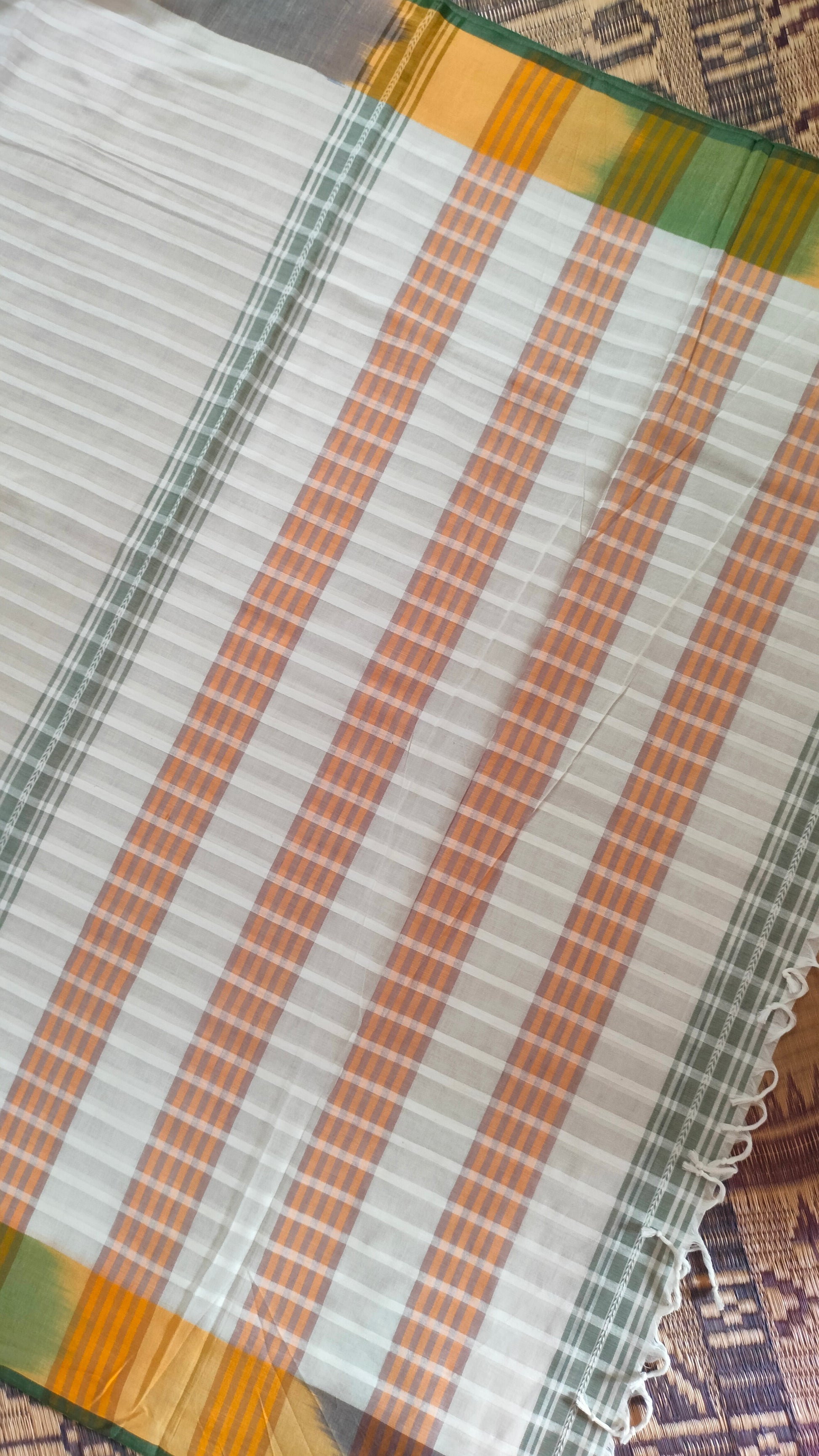 Dhonekhali handloom cotton saree with a striped body in alternating off-white and cream tones, complemented by a vibrant multi-hued border in green, purple, and yellow abstract patterns. Finished with tassel details at the pallu.