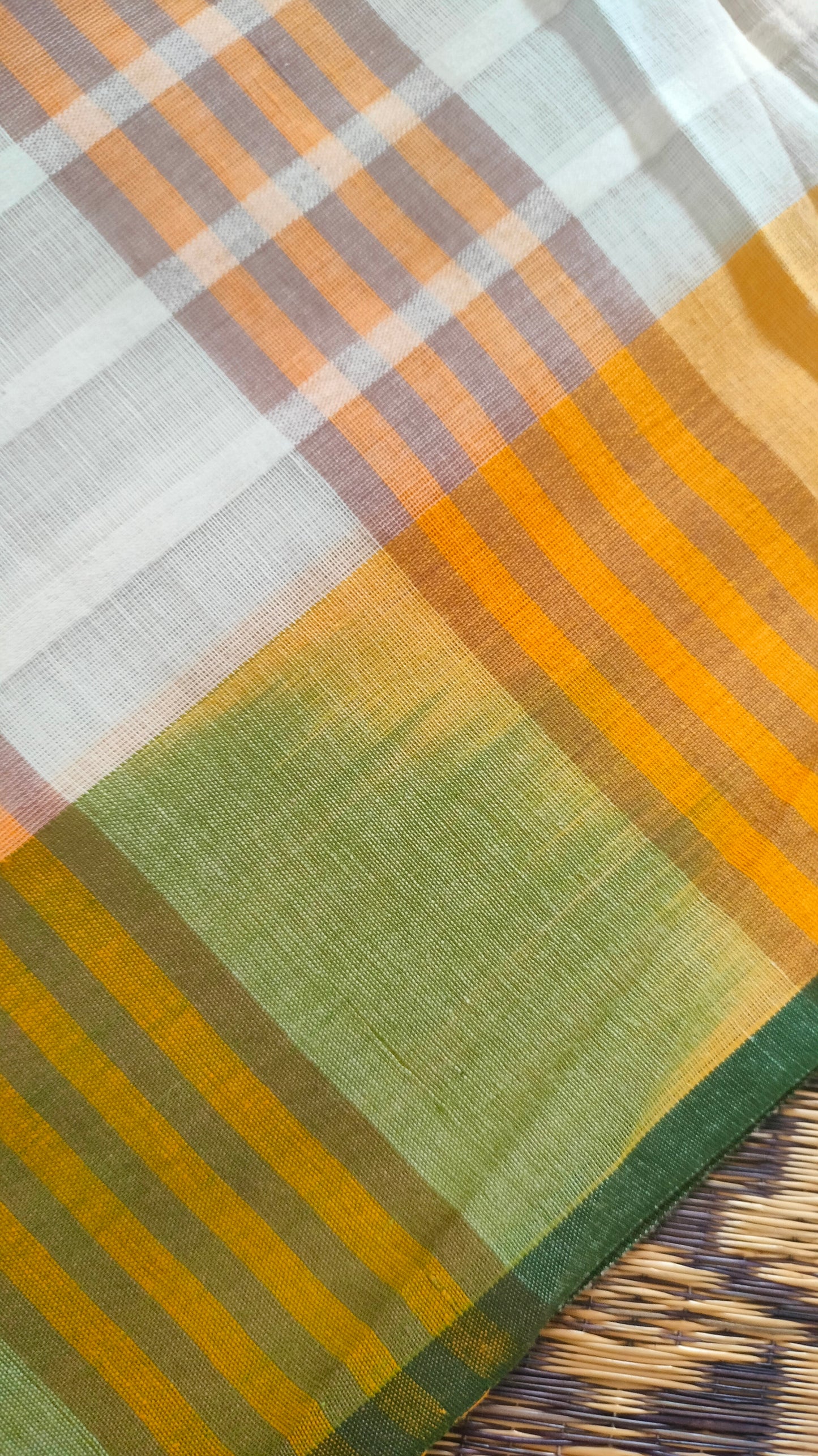 Dhonekhali handloom cotton saree with a striped body in alternating off-white and cream tones, complemented by a vibrant multi-hued border in green, purple, and yellow abstract patterns. Finished with tassel details at the pallu.