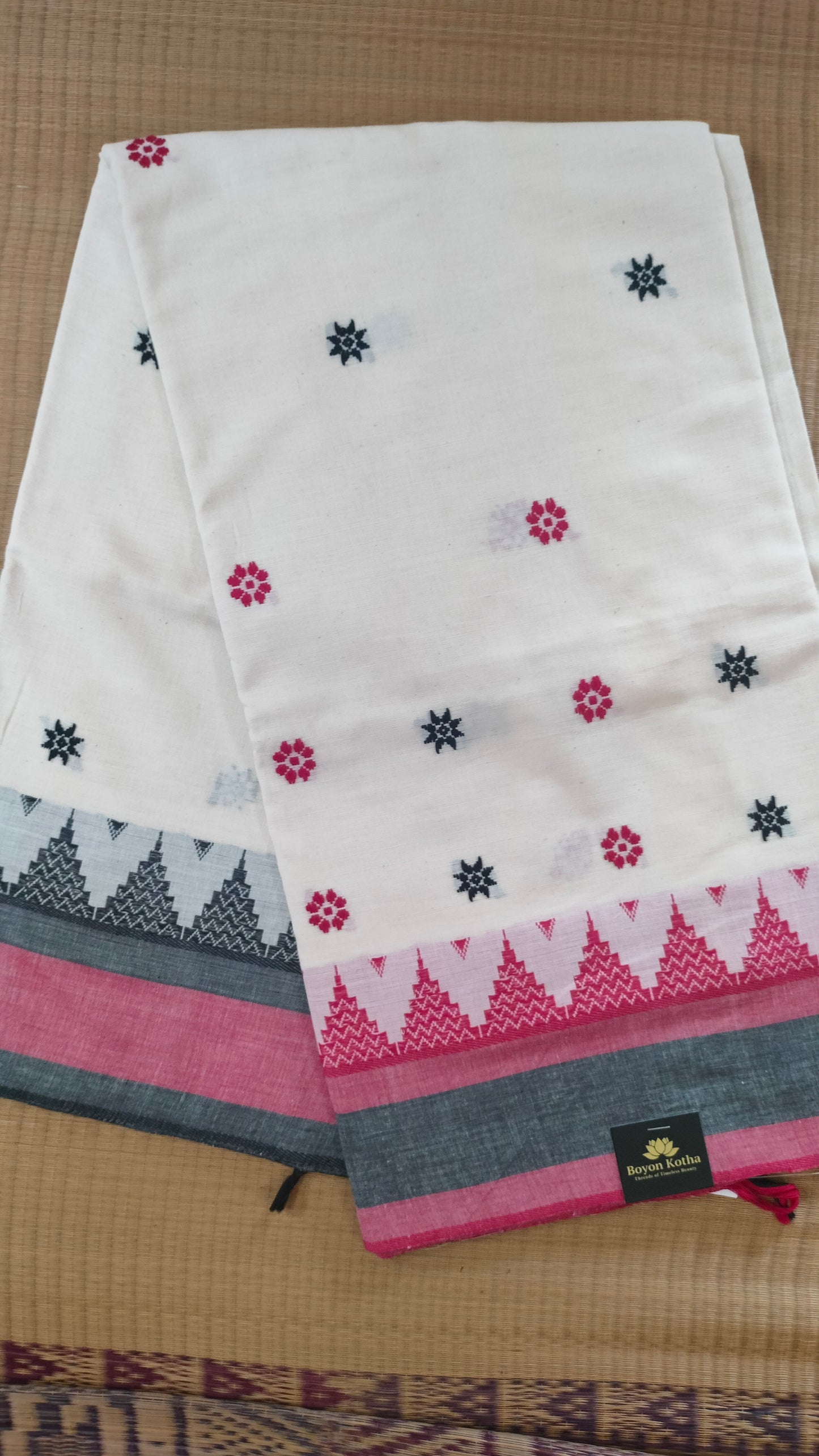 Dhonekhali handloom saree from Bengal, featuring a pristine white body adorned with red and black woven butis throughout. The dual borders—deep red at the lower edge and bold black at the upper edge—showcase intricate temple motifs, while the pallu ends with tassels. 
