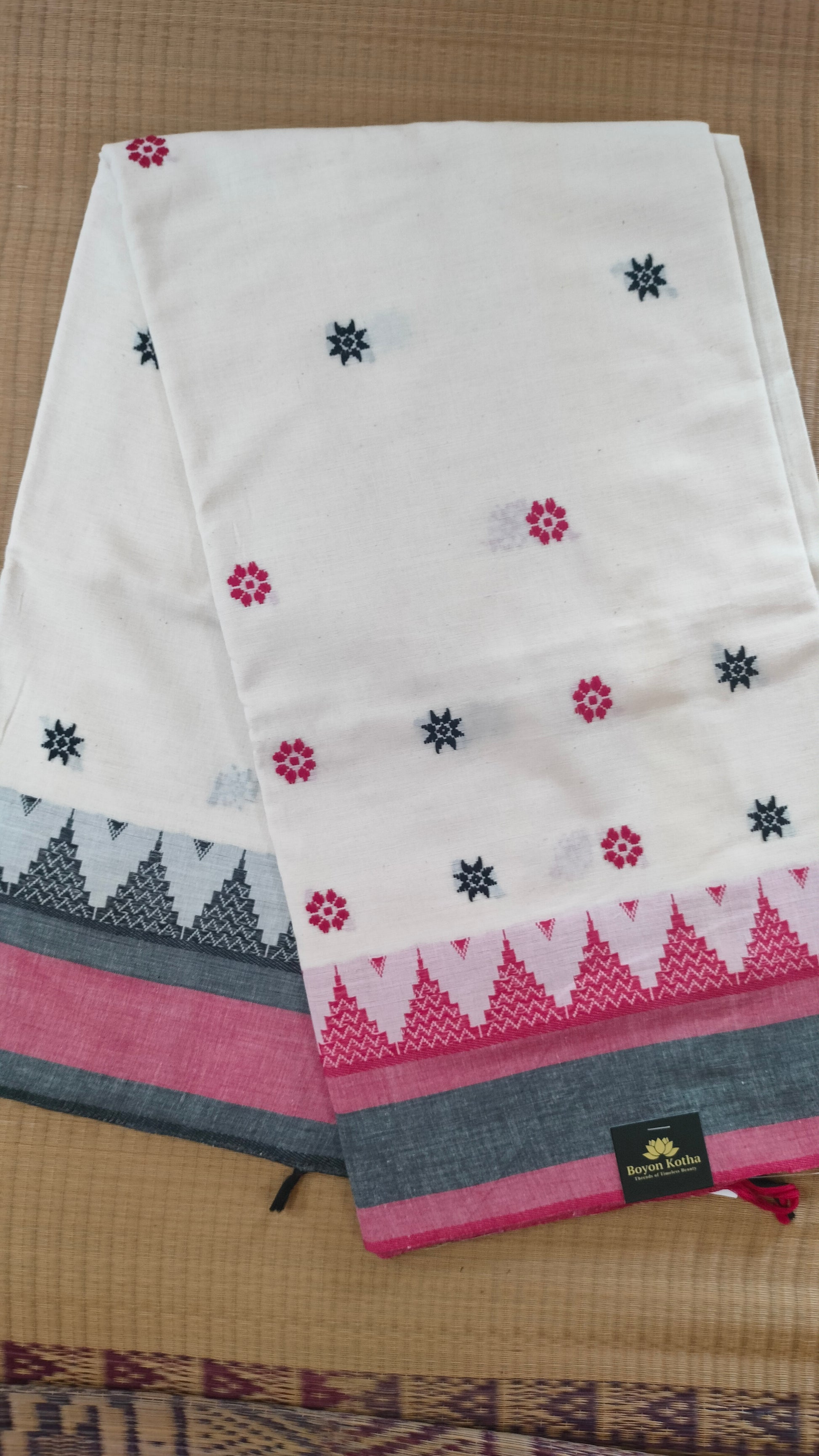Dhonekhali handloom saree from Bengal, featuring a pristine white body adorned with red and black woven butis throughout. The dual borders—deep red at the lower edge and bold black at the upper edge—showcase intricate temple motifs, while the pallu ends with tassels. 