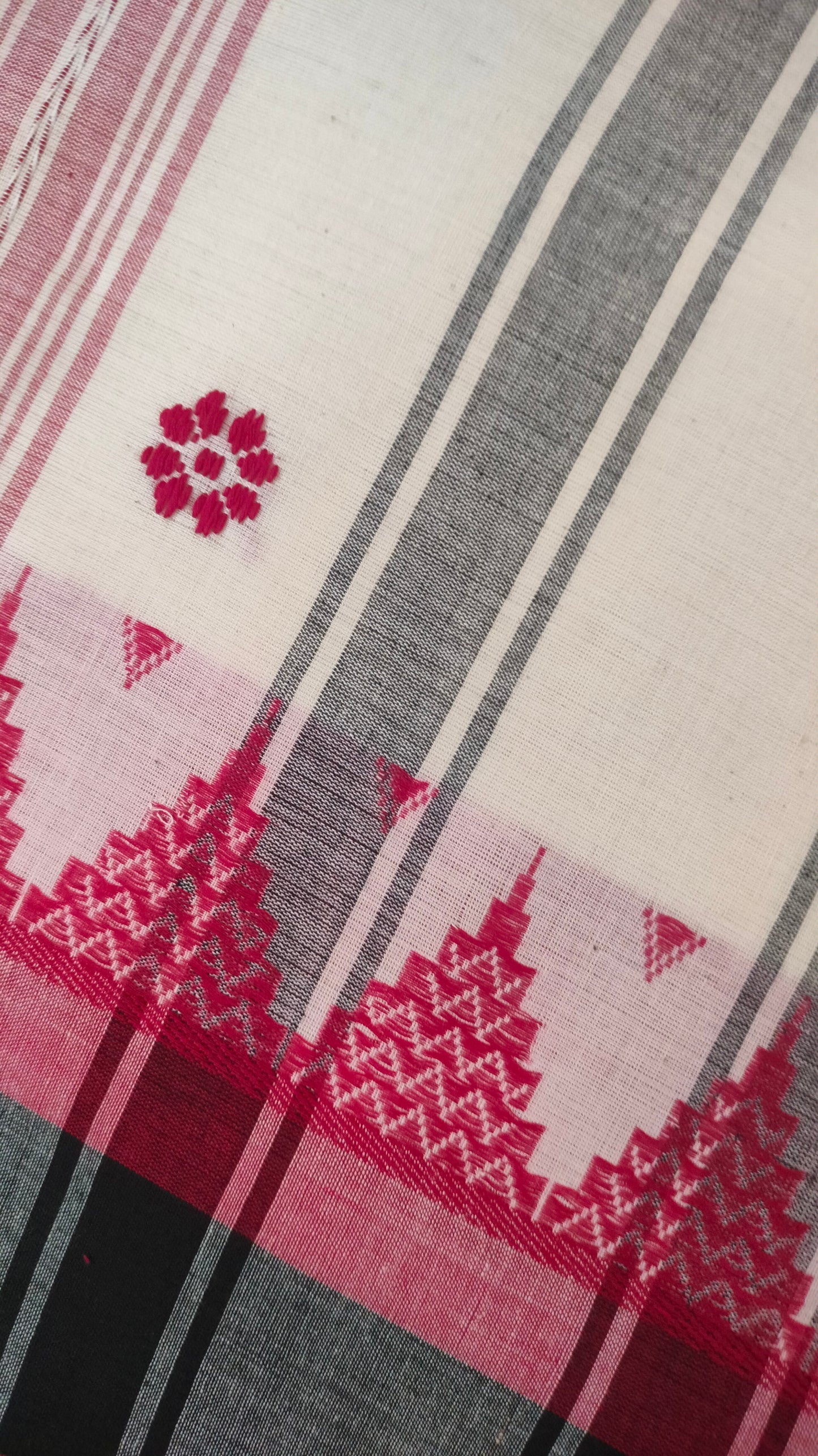 Dhonekhali handloom saree from Bengal, featuring a pristine white body adorned with red and black woven butis throughout. The dual borders—deep red at the lower edge and bold black at the upper edge—showcase intricate temple motifs, while the pallu ends with tassels. 