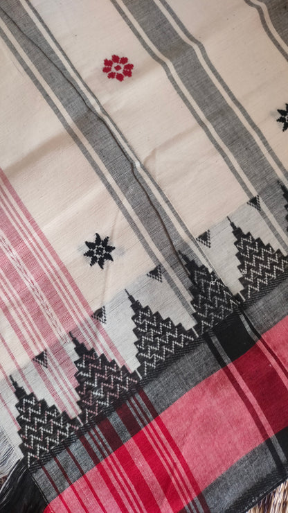 Close-up of Dhonekhali handloom saree from Bengal, featuring a pristine white body adorned with red and black woven butis throughout. The dual borders—deep red at the lower edge and bold black at the upper edge—showcase intricate temple motifs, while the pallu ends with tassels. 