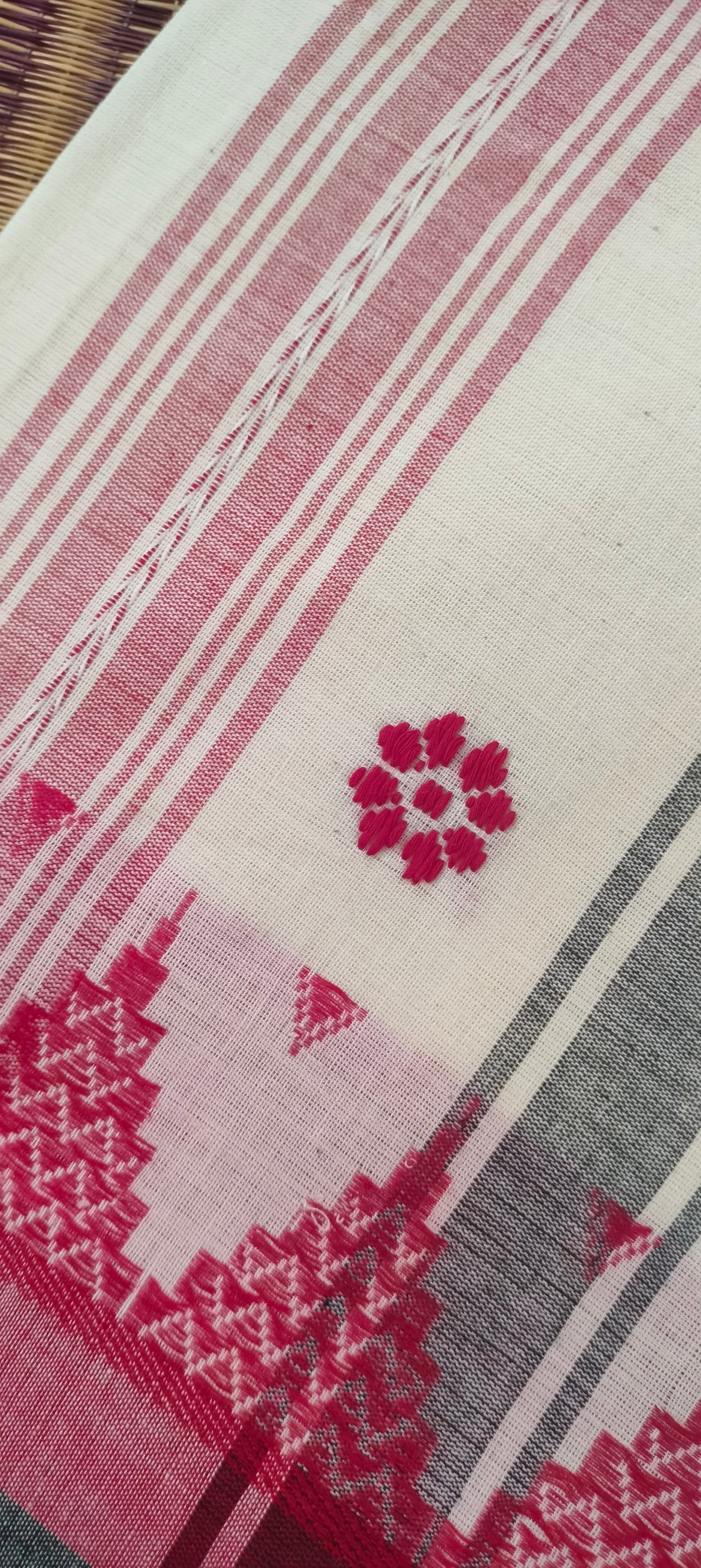 Close-up of Dhonekhali handloom saree from Bengal, featuring a pristine white body adorned with red and black woven butis throughout. The dual borders—deep red at the lower edge and bold black at the upper edge—showcase intricate temple motifs, while the pallu ends with tassels. 