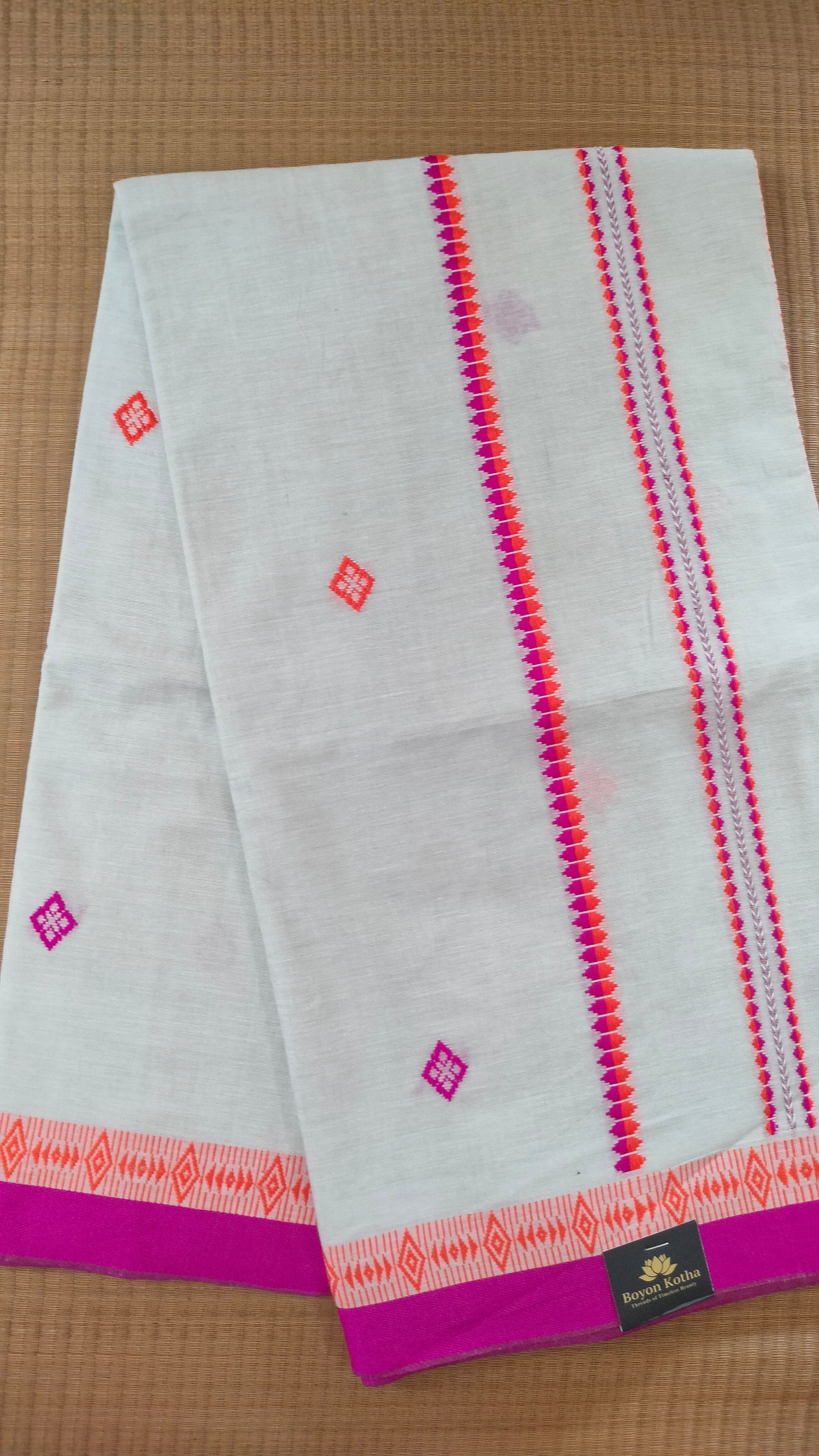 A white Dhonekhali handloom cotton saree with orange and pink woven motifs and bands on the saree. The border of the saree is pink with the inner edge having orange motifs.