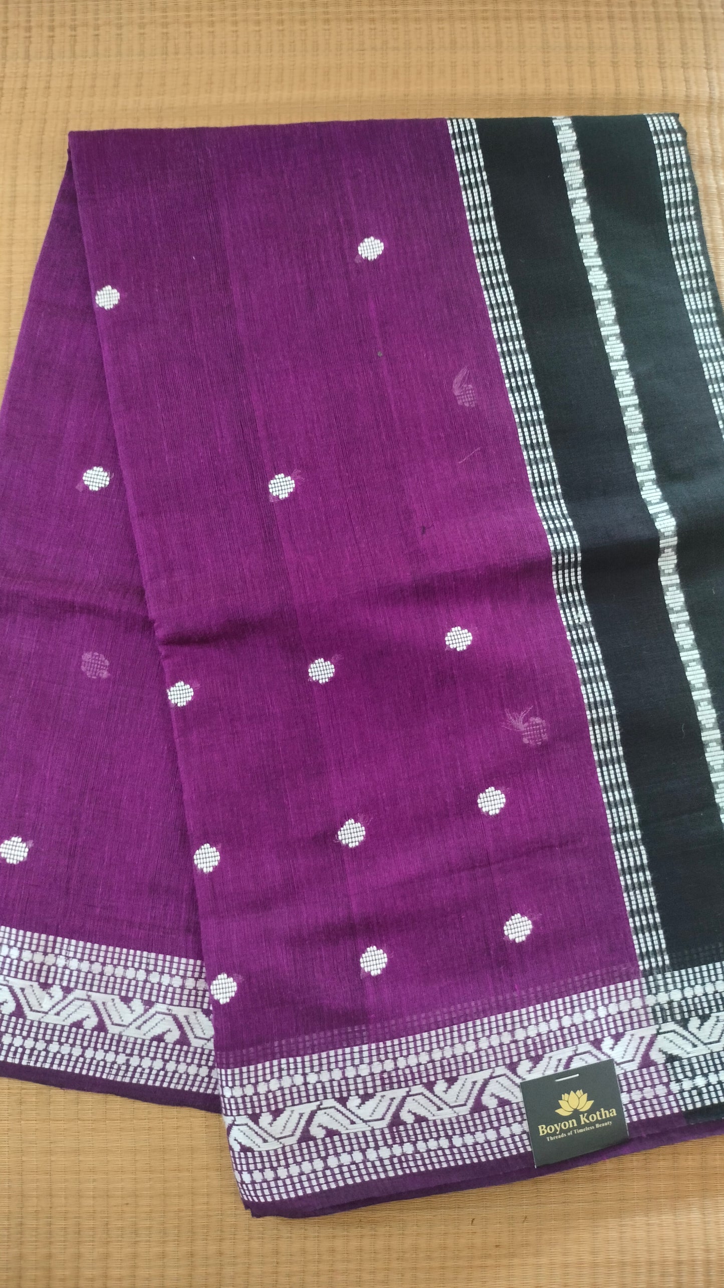 Purple Dhonekhali handloom cotton saree with woven white motifs across the body and the border with a black pallu that has woven white vertical stripes.