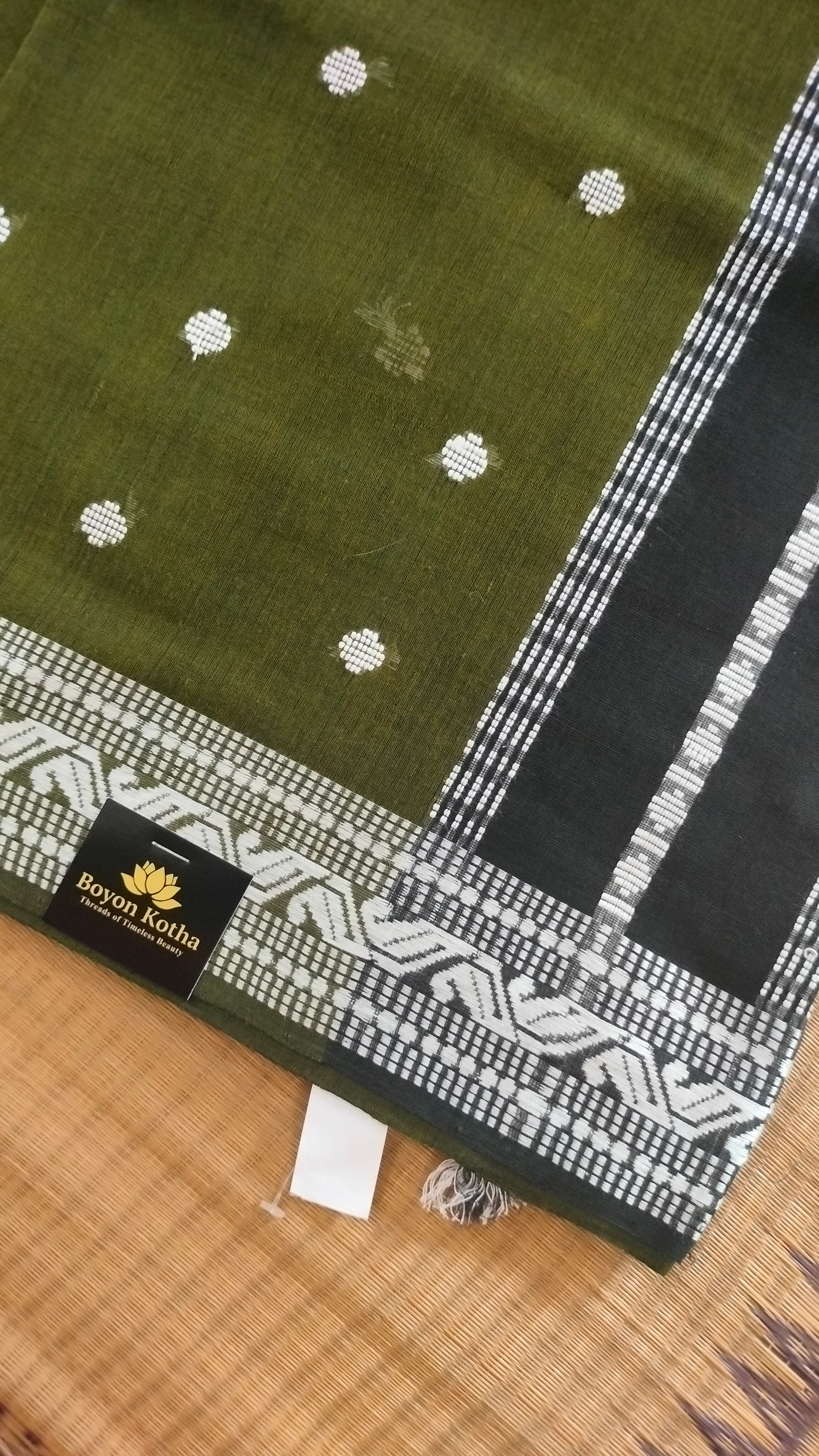 Olive Green Dhonekhali handloom cotton saree with woven white motifs across the body and the border with a black pallu that has woven white vertical stripes.