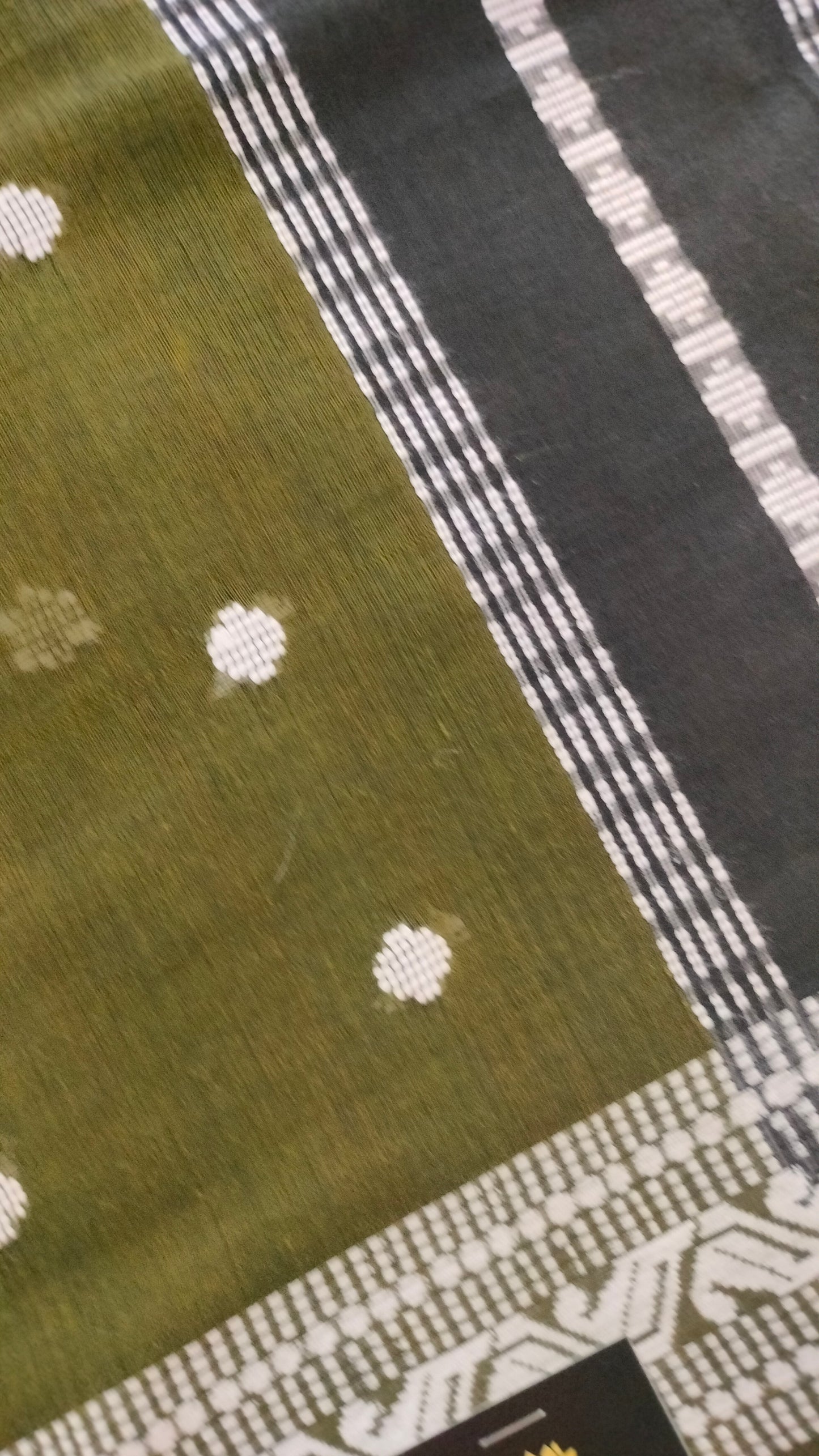 Olive Green Dhonekhali handloom cotton saree with woven white motifs across the body and the border with a black pallu that has woven white vertical stripes.