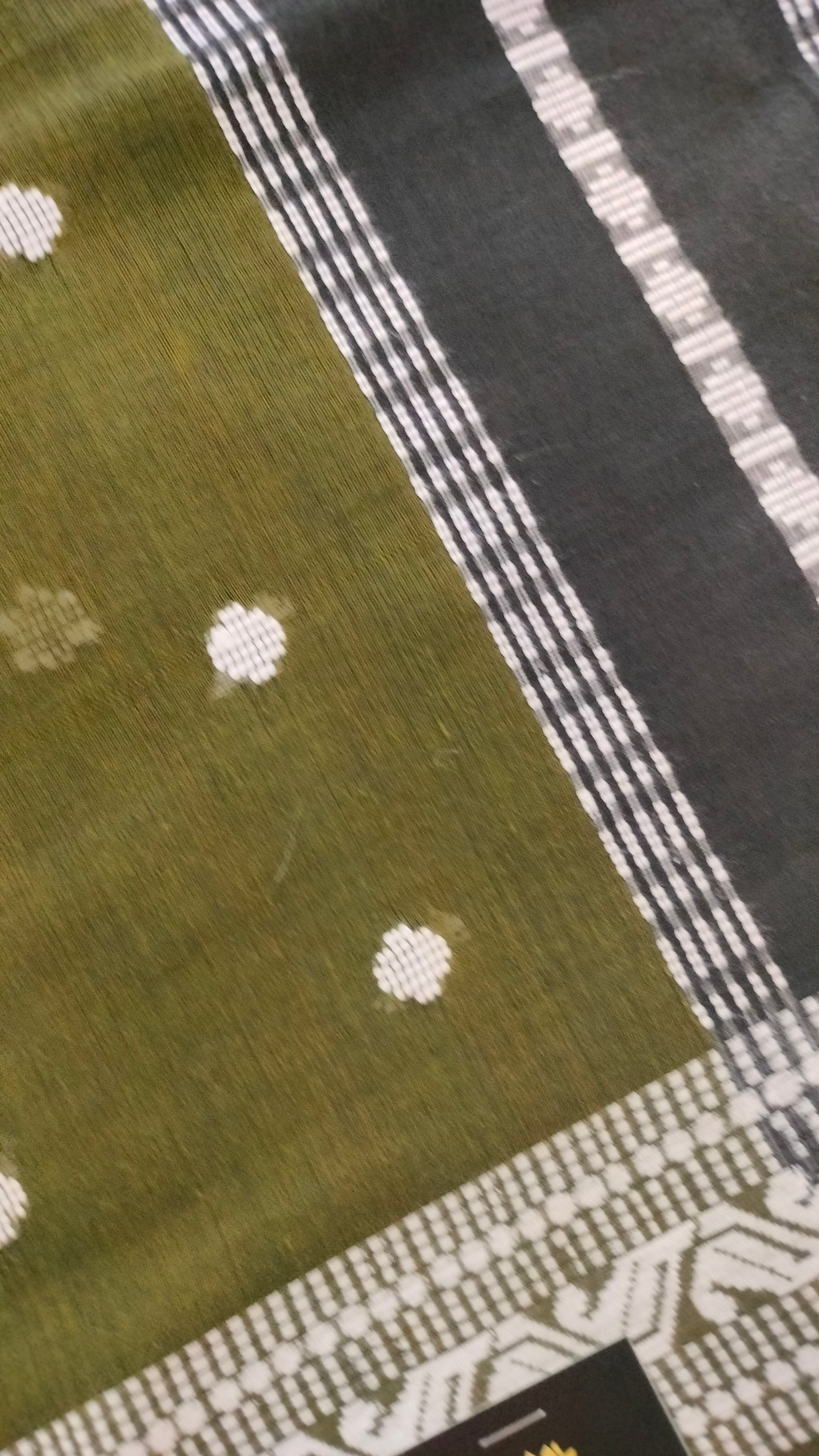 Olive Green Dhonekhali handloom cotton saree with woven white motifs across the body and the border with a black pallu that has woven white vertical stripes.
