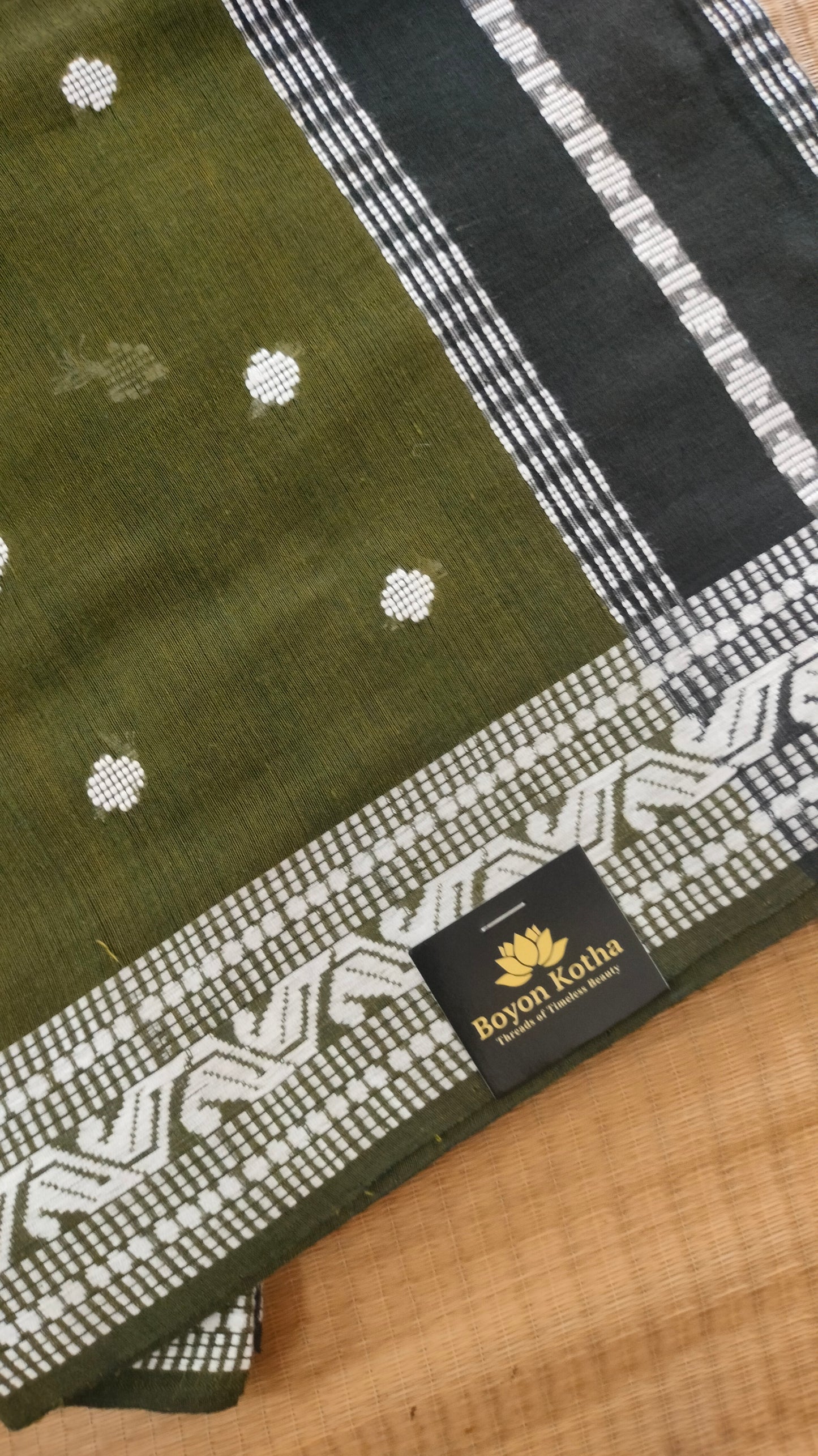 Olive Green Dhonekhali handloom cotton saree with woven white motifs across the body and the border with a black pallu that has woven white vertical stripes.