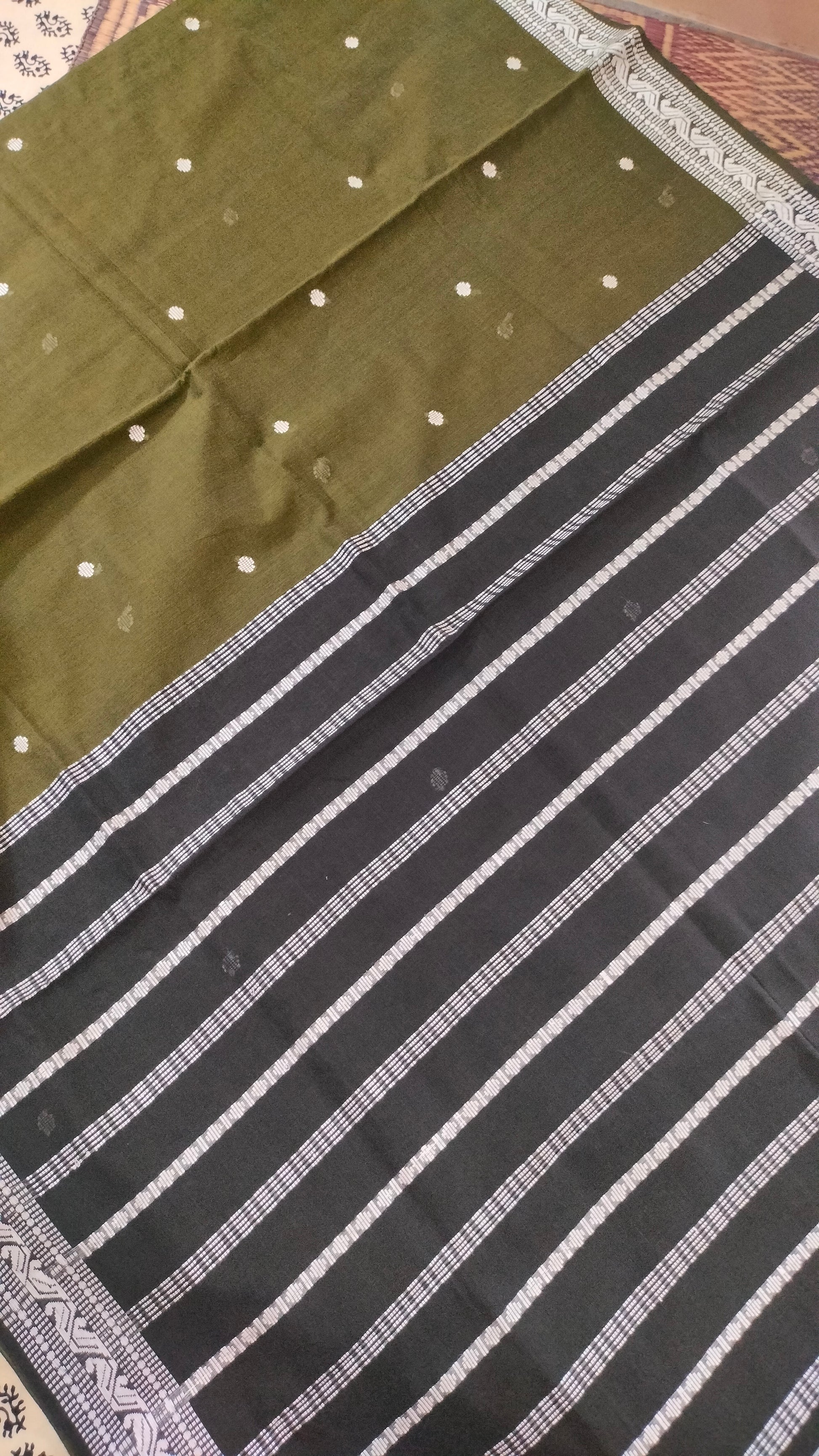Olive Green Dhonekhali handloom cotton saree with woven white motifs across the body and the border with a black pallu that has woven white vertical stripes.